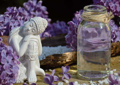 Massagegutschein mit Buddhafigur, Blüten und Glas als Bildmotiv